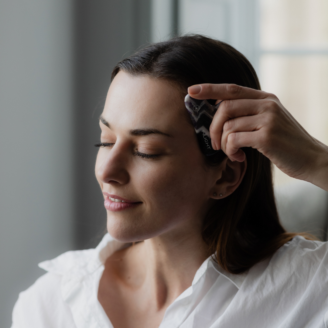 woman with brown hair using the inlight beauty amethyst gua sha tool on her temple