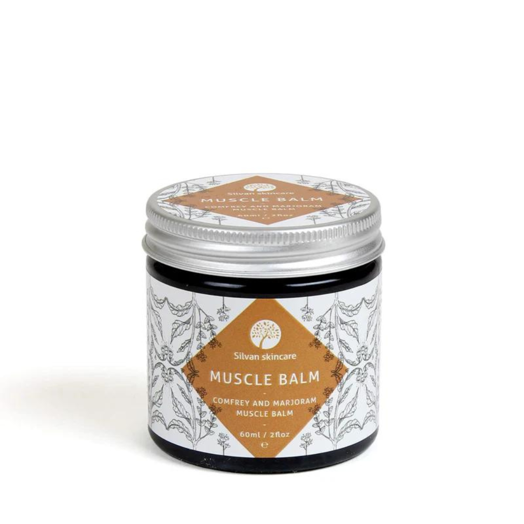 A glass jar of silvan skincare Muscle balm. The small jar has an aluiminium lid and the label is white with a dark orange diamond surrounded with botanical illustrations