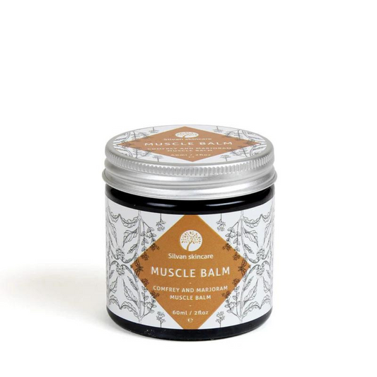 A glass jar of silvan skincare Muscle balm. The small jar has an aluiminium lid and the label is white with a dark orange diamond surrounded with botanical illustrations