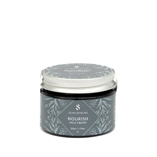 A glass jar of silvan skincare nourish face cream. The small jar has an aluiminium lid and the labels are in dark blue with botanical illustrations