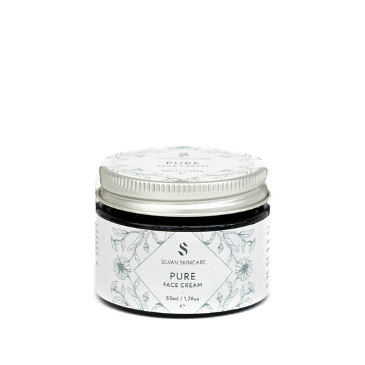 A glass jar of silvan skincare pure face cream. The small jar has an aluiminium lid and the labels are in white  with blue botanical illustrations
