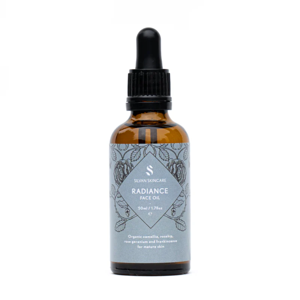 Silvan Skincare Radiance Face Oil in an amber glass bottle with a blue label, white text listing the product and brand and black botanical illustrations. The bottle is against a white backdrop. Natural Body Oil