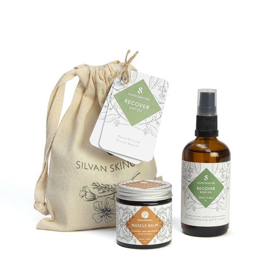  Silvan Skincare recover Gift Set. Vegan gifts. The gift set is photographed on a white background. You can see the branded muslin cloth bag in the background. In the foreground you can see the muscle balm and recover body oil. 