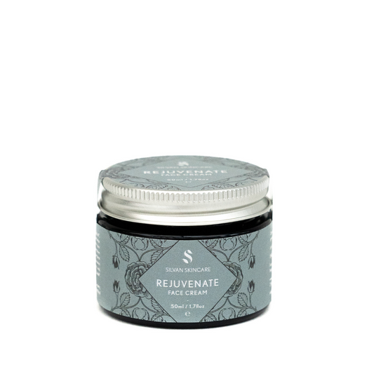 A glass jar of silvan skincare rejuvenate face cream. The small jar has an aluminium lid and the labels are in a grey/blue with black botanical illustrations
