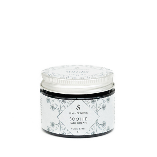 A glass jar of silvan skincare soothe face cream. The small jar has an aluminium lid and the labels are in a very pale blue with dark blue botanical illustrations