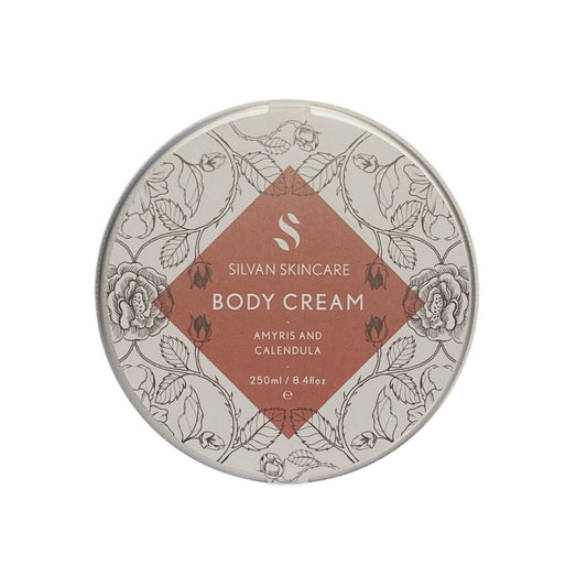 aluminium tin filled with a creamy body moisturiser inside. the label on the tin features etches of the natural ingredients within the body cream and a dusky red diamond shape which has white text stating the name of the product silvan skincare body cream with amyris and calendula