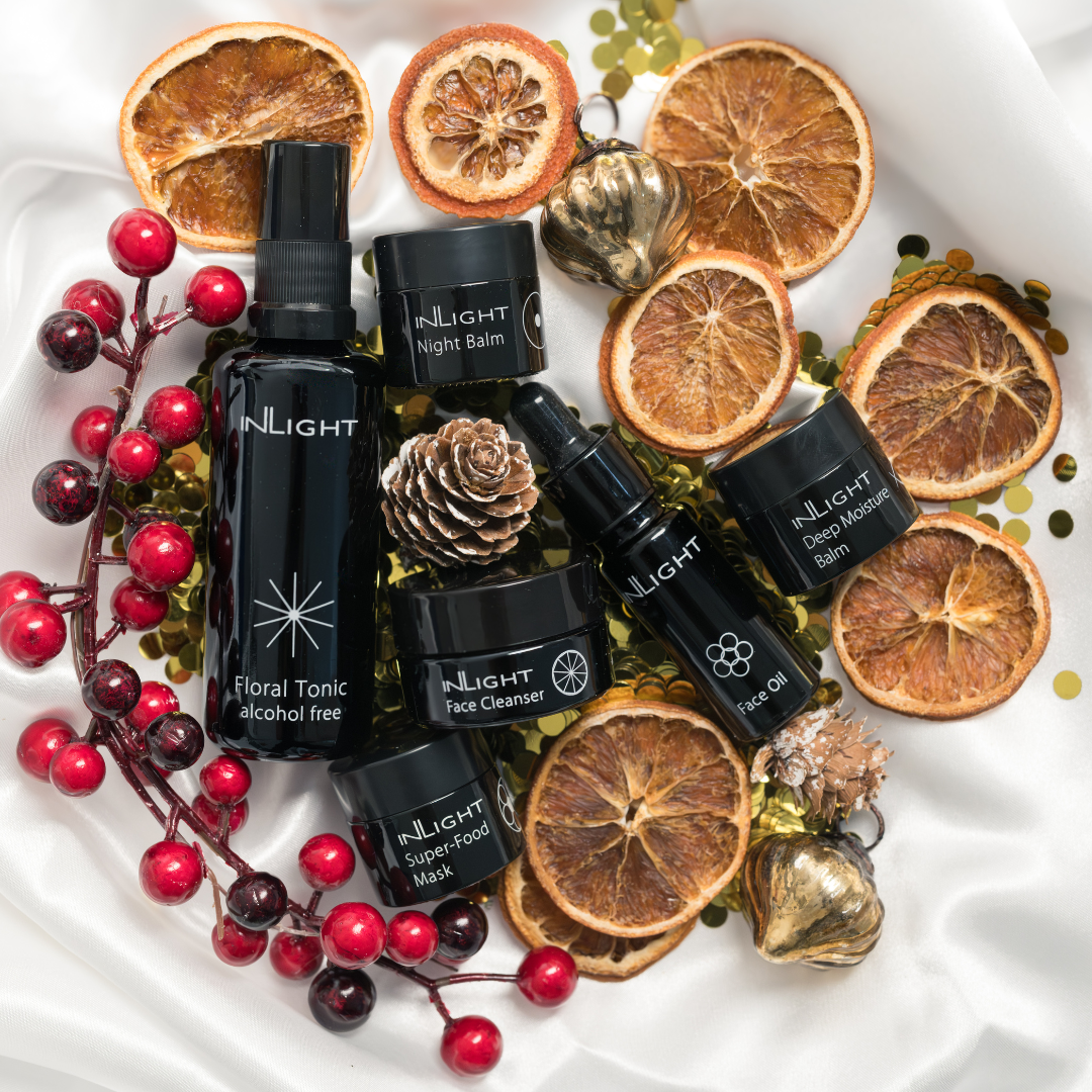 dried orange slices, red berries, gold bauble, pine cones and a bed of round gold glitter is the base for the glass bottles of inlight beauty's organic skincare products from the ultimate facial set to be sitting on in a juxtaposed group
