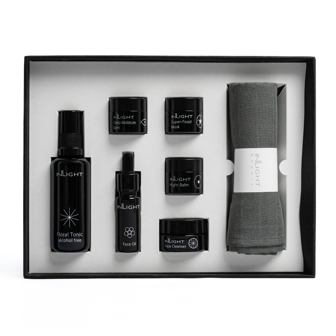 top down view of open gift set box of inlight beauty's ultimate facial set, a full set of their organic facial skincare range in miniature featuring glass miron bottles of flora tonic, face oil, deep moisture balm, superfood mask, night balm, face cleanser