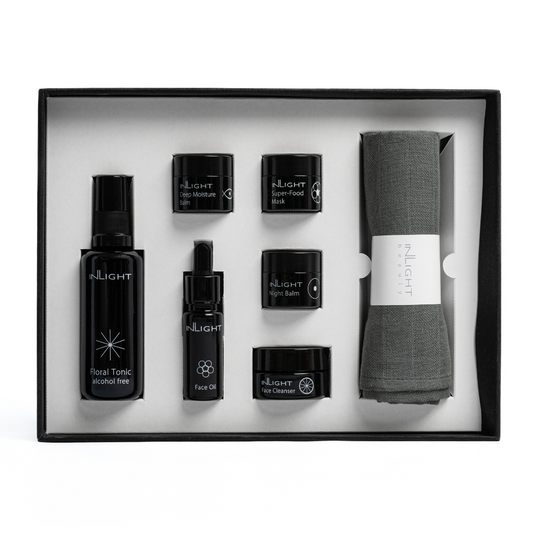 top down view of open gift set box of inlight beauty's ultimate facial set, a full set of their organic facial skincare range in miniature featuring glass miron bottles of flora tonic, face oil, deep moisture balm, superfood mask, night balm, face cleanser