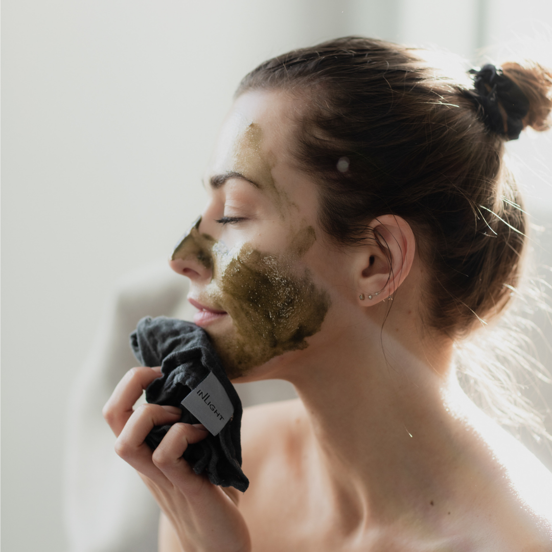 woman with brown hair tied back wiping away inlight beauty's superfood face mask with a grey muslin cloth