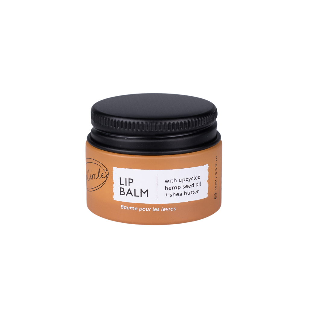 A pot of the Upcircle Lip balm. The product is in an orange glass jar with a black aluminium lid. The brand and product info are listed in black and white text and highlights the upcycled ingredients.