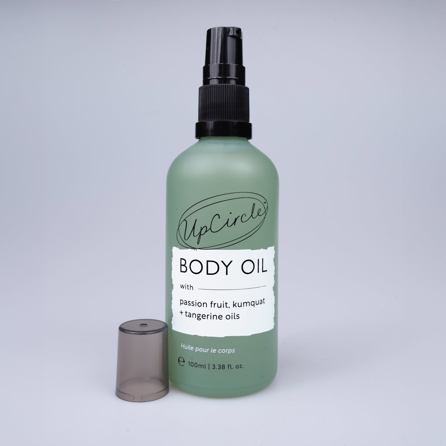 green glass bottle of upcircle body oil with a black pump and the frosted black/grey lid leaning against the bottle