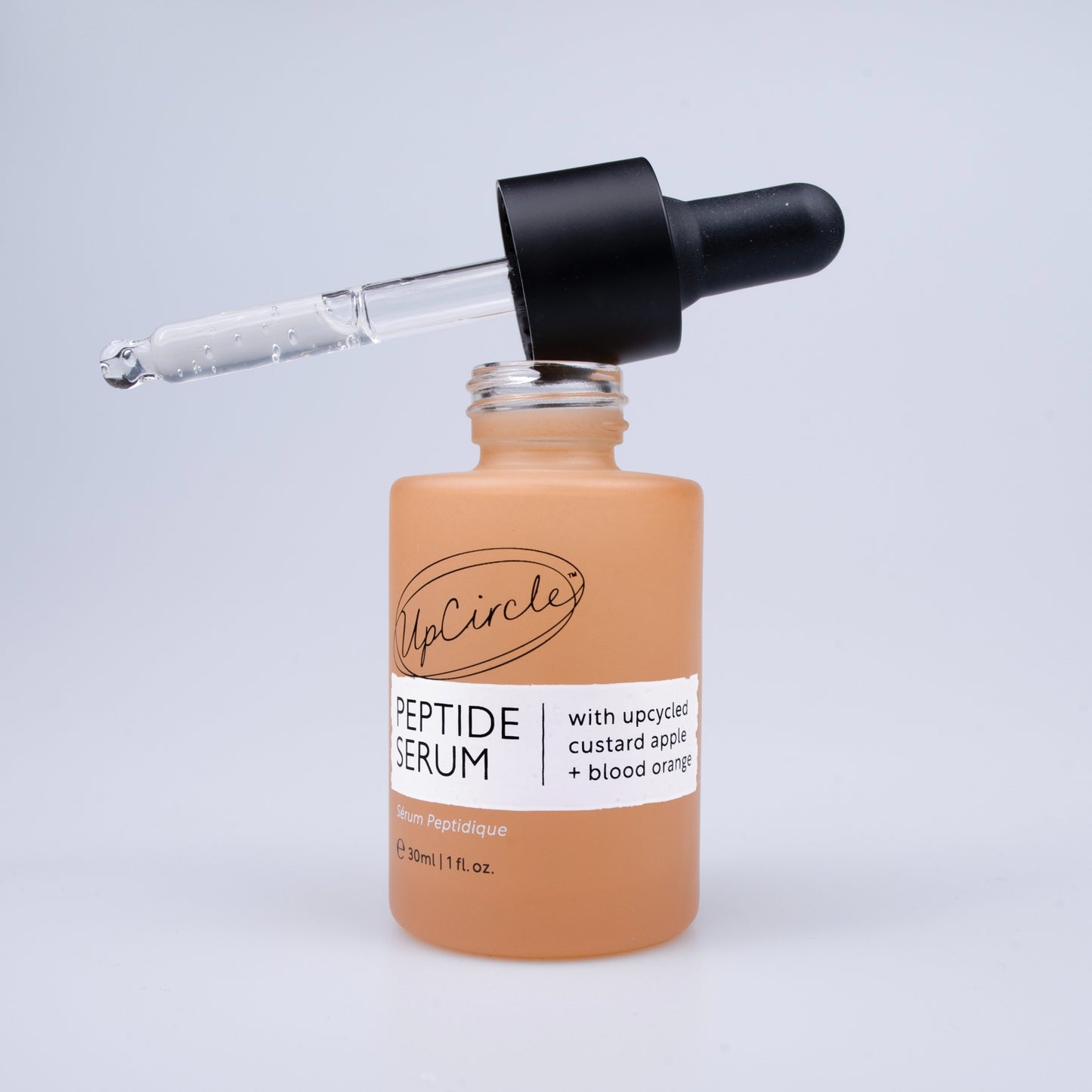 upcircle peptide serum bottle with the pipette dropper balancing on top which is full of serum