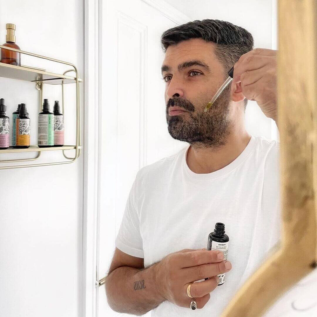 man with beard looking into mirror and applying beard oil