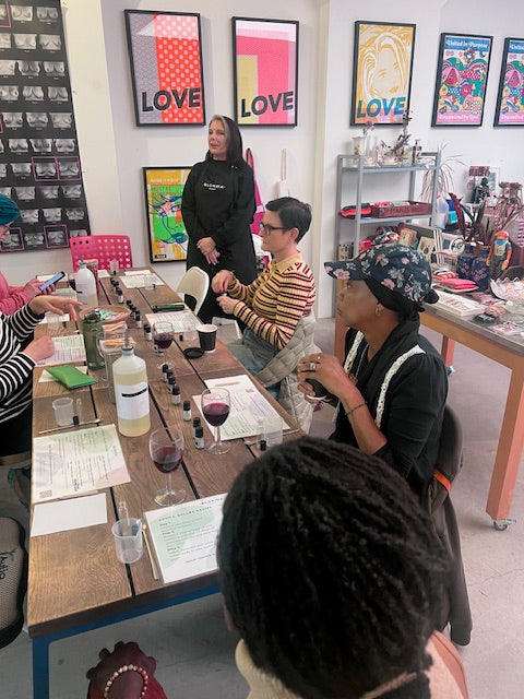 teacher guiding a group of people sitting around a wooden table how to blend an aromatherapy fragrance/perfume blend