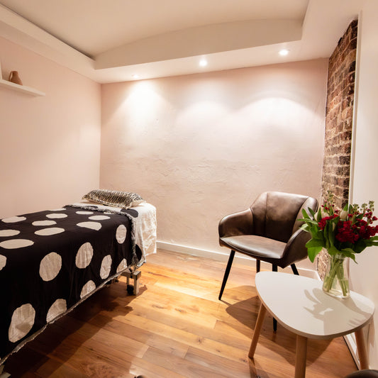 Room with a massage table covered by a black and white polka dot sheet, a chair, and a small table with flowers.