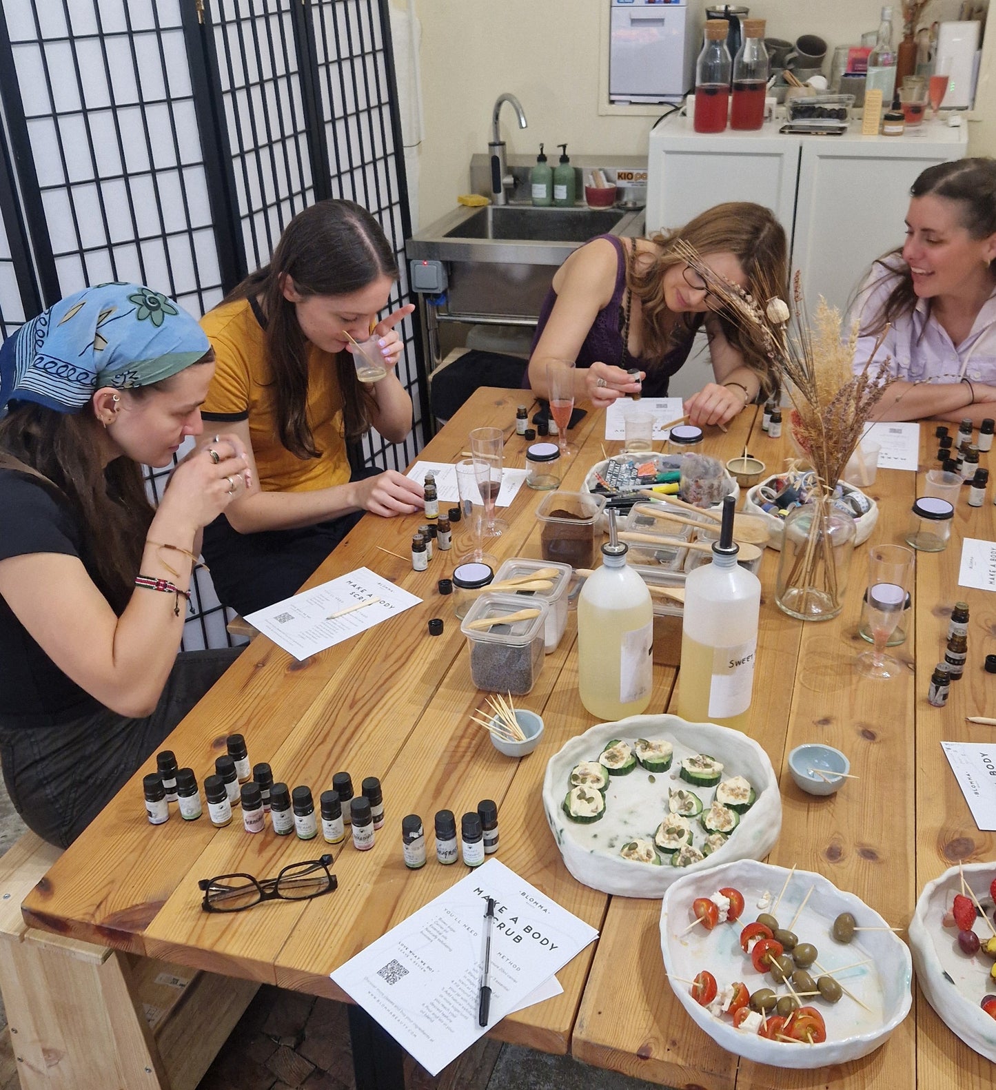 four women sitting around a table with natural skincare ingredients hand making body scrubs