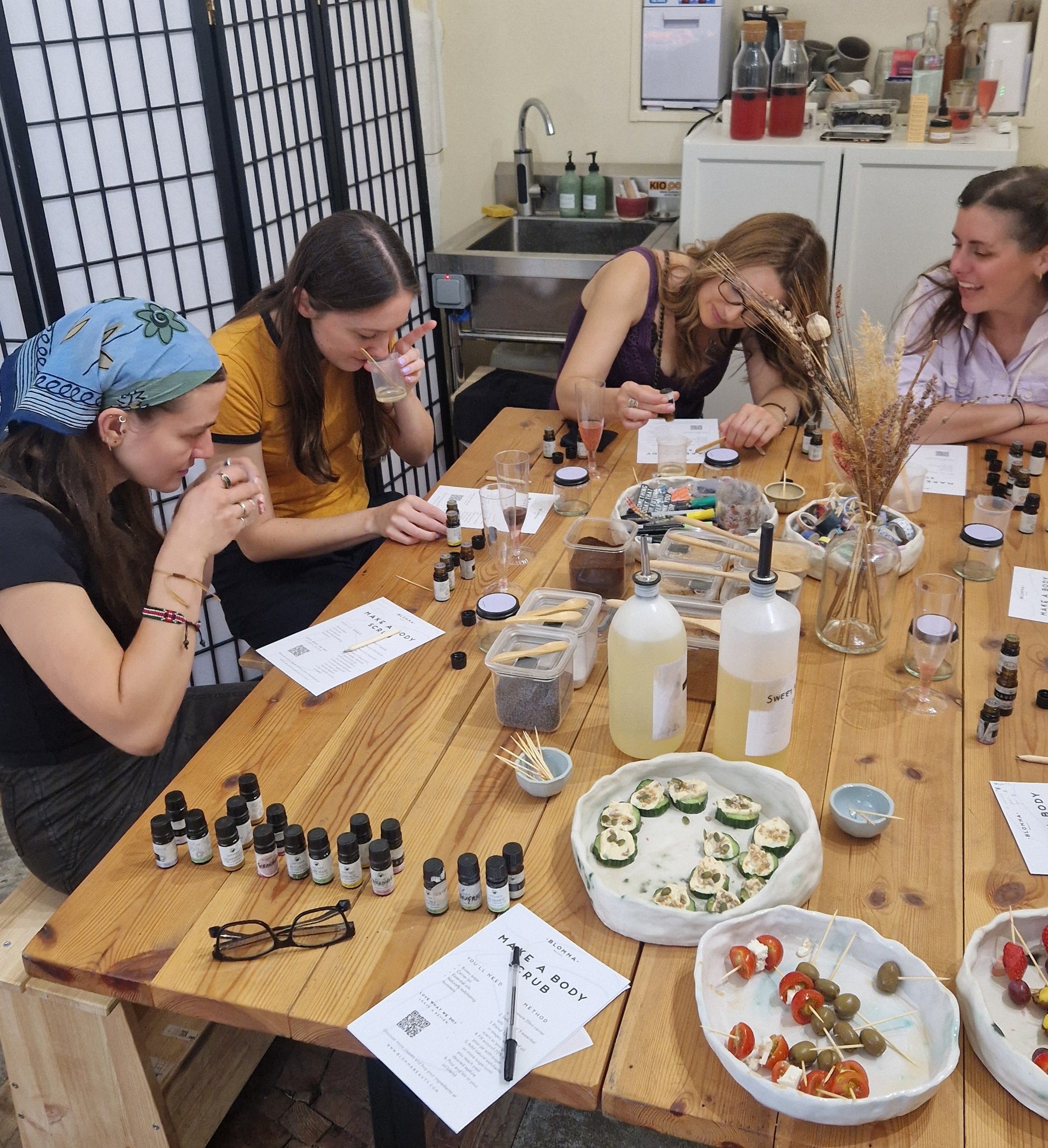 four women sitting around a table with natural skincare ingredients hand making body scrubs