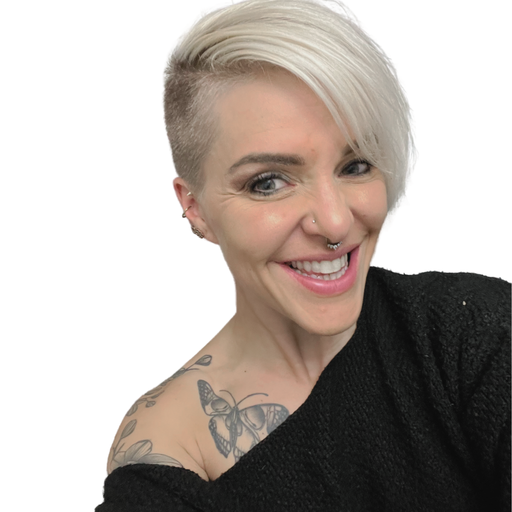 essjay hartsorn founder of bomonde mineral make up which is vegan and cruelty free. in the photo she has short bleach blonde hair with one side of her head shaved. she is wearing a black one shoulder jumper and you can see butterfly and nature tattoos on the shoulder that is exposed.