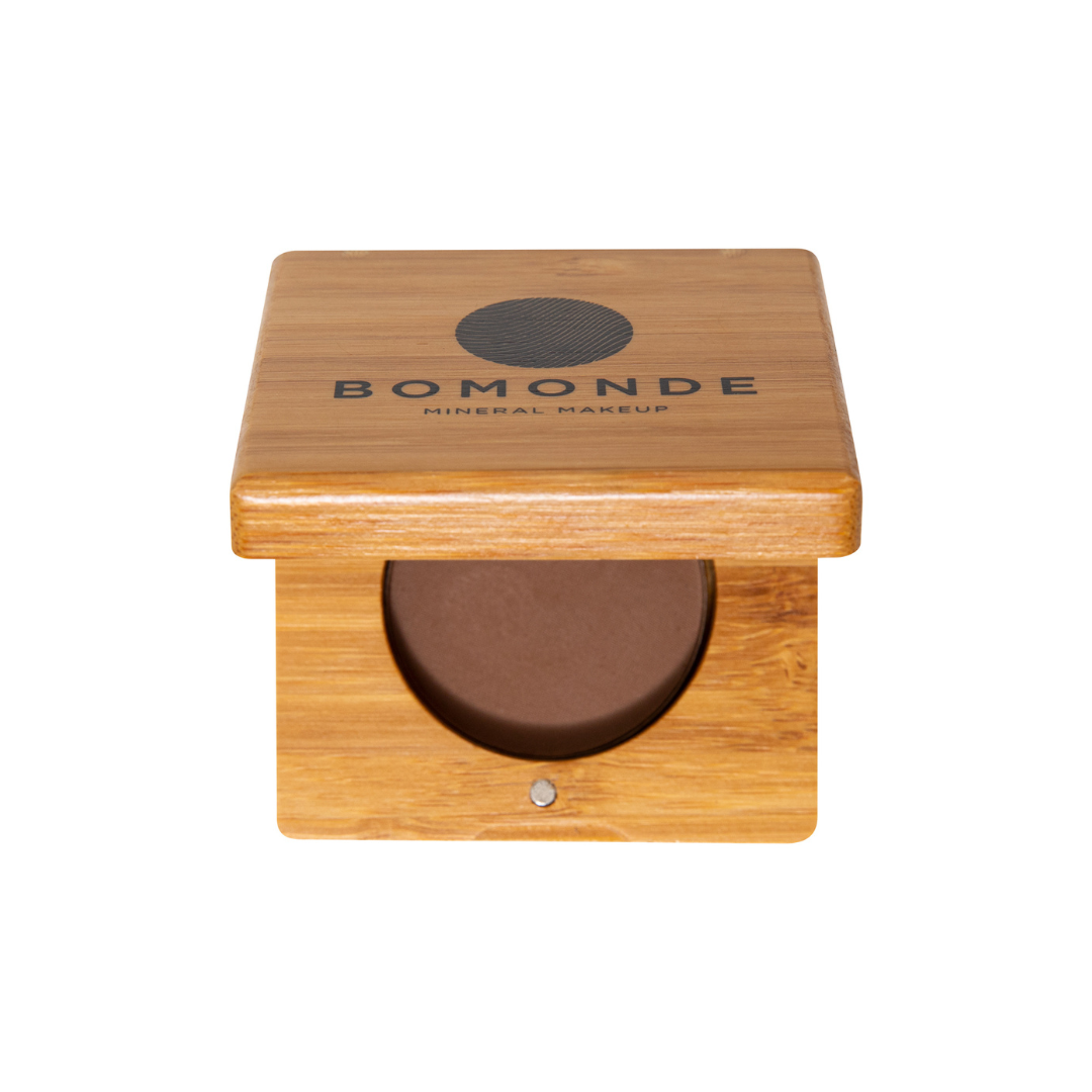 an aerial view of bomonde mineral make up eyebrow palette in brown. the bamboo compact case is angled open. you can see the black text on the top of the bamboo refillable make up compact which reads 'bomonde mineral make up' and you can see the round section for placing the eyebrow powder in to