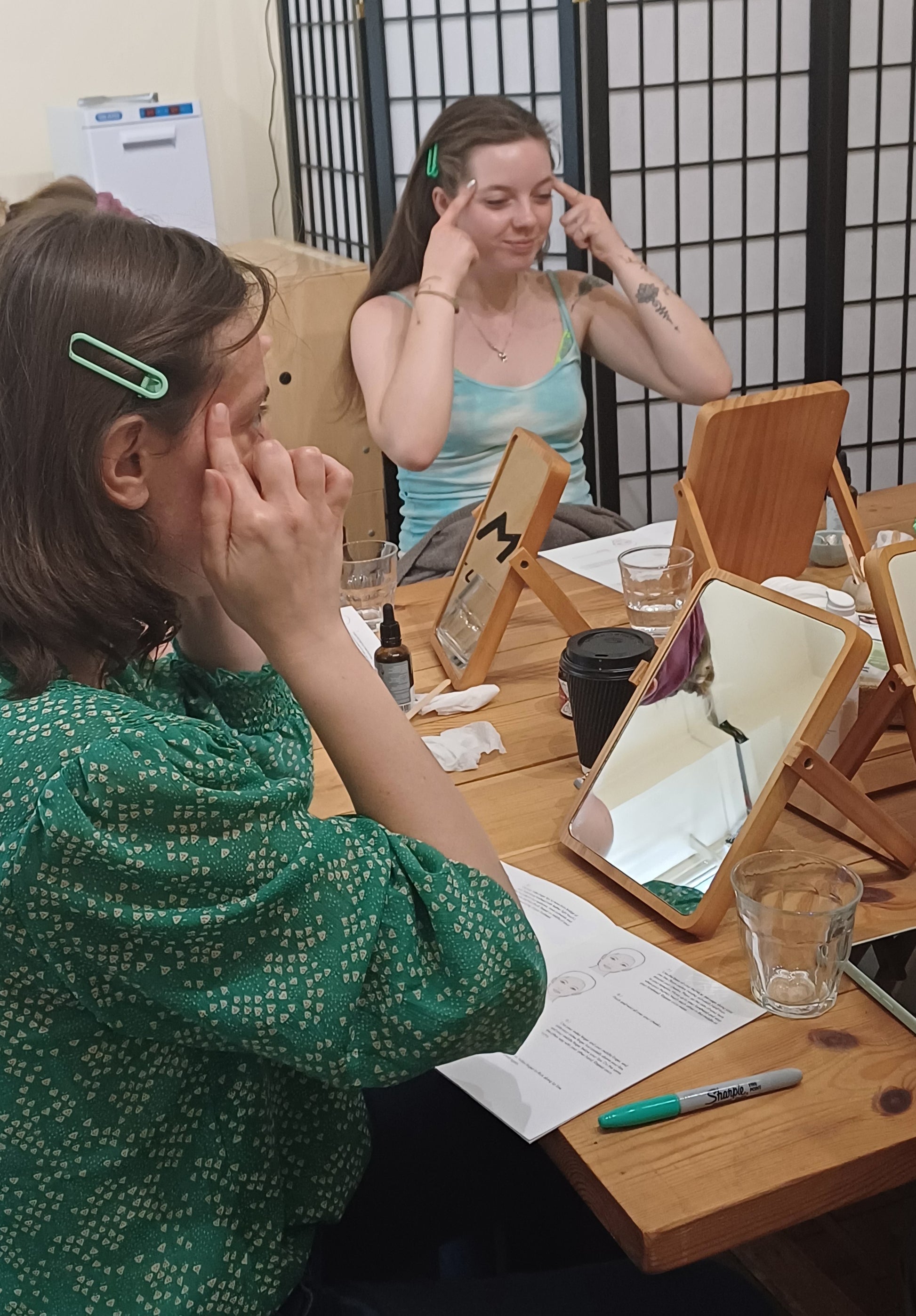 two women looking into mirrors while they are doing face yoga
