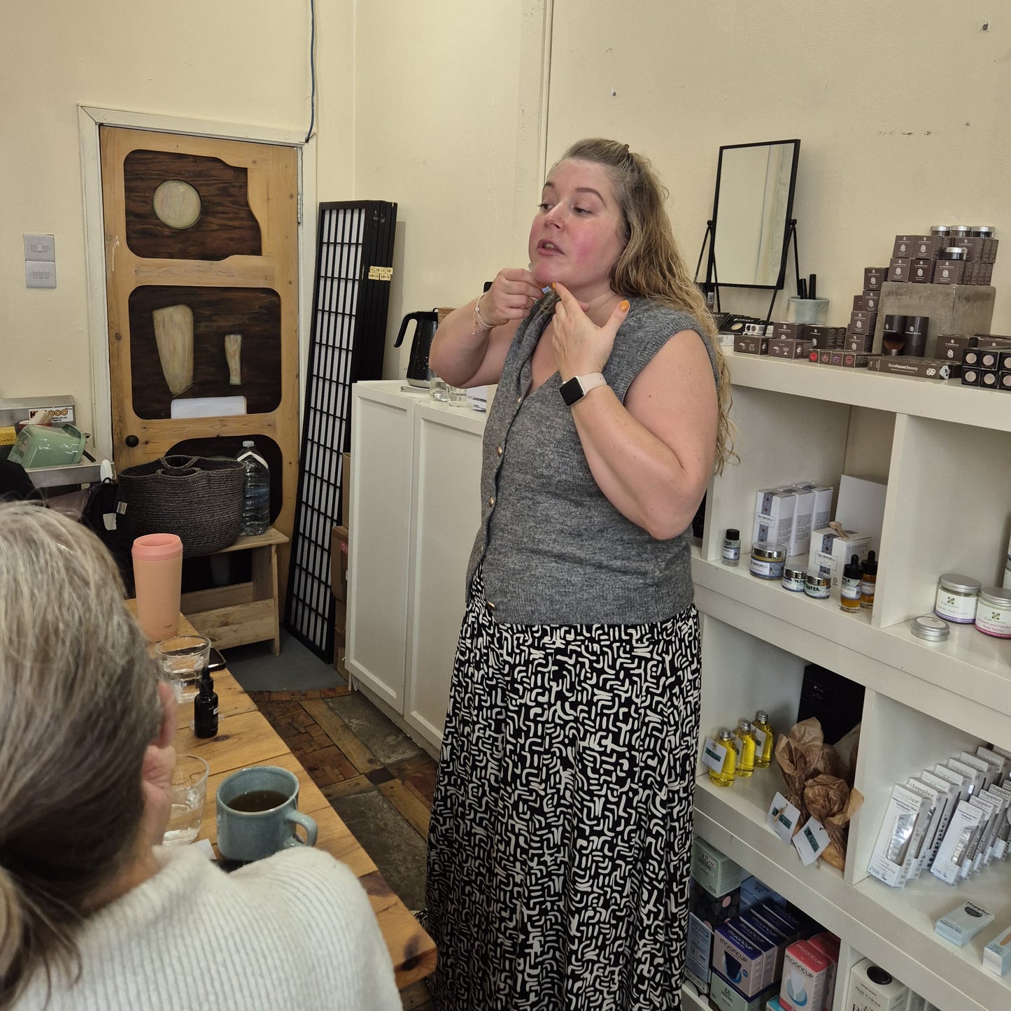Woman standing in a room with shelves and a mirror, demonstrating how to use face cups in a skincare ritual