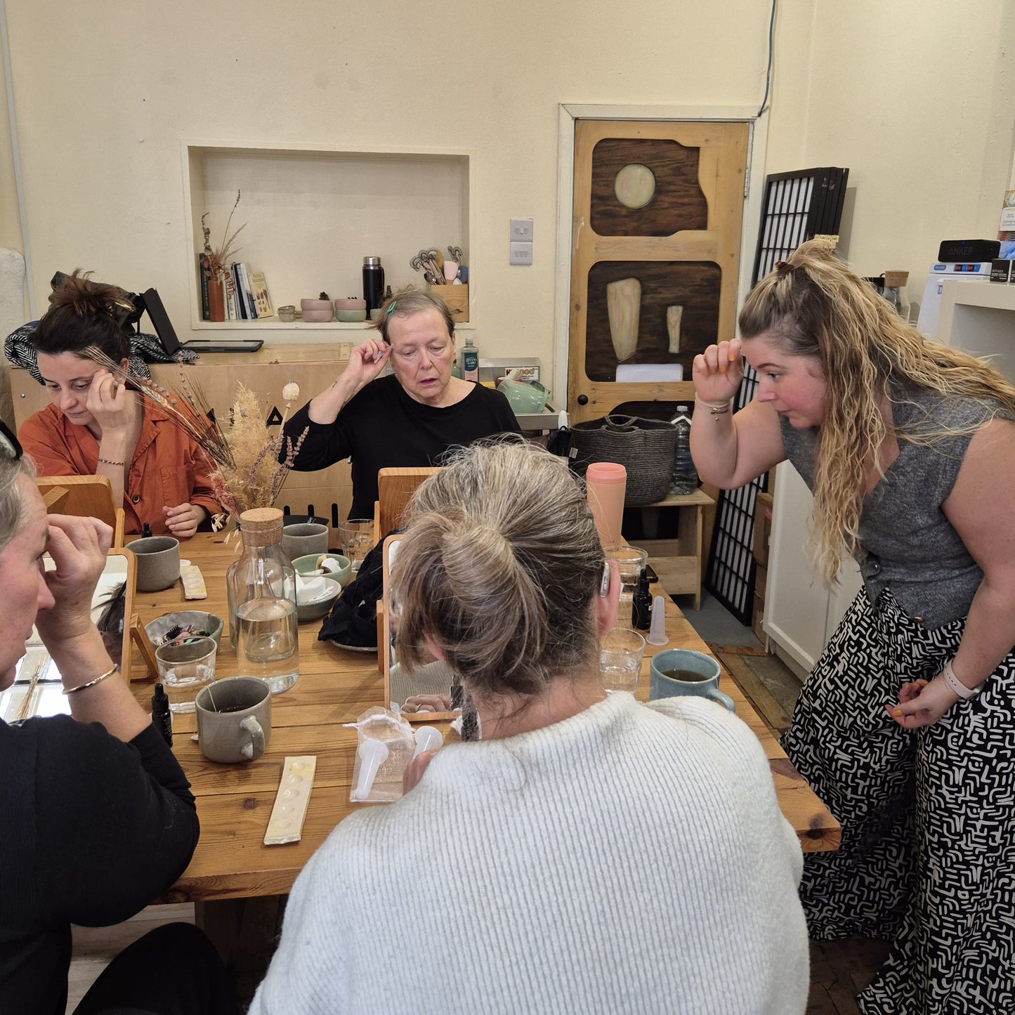 Group of people sitting around a wooden table in a casual setting, learning about organic skincare and how to use facial cups