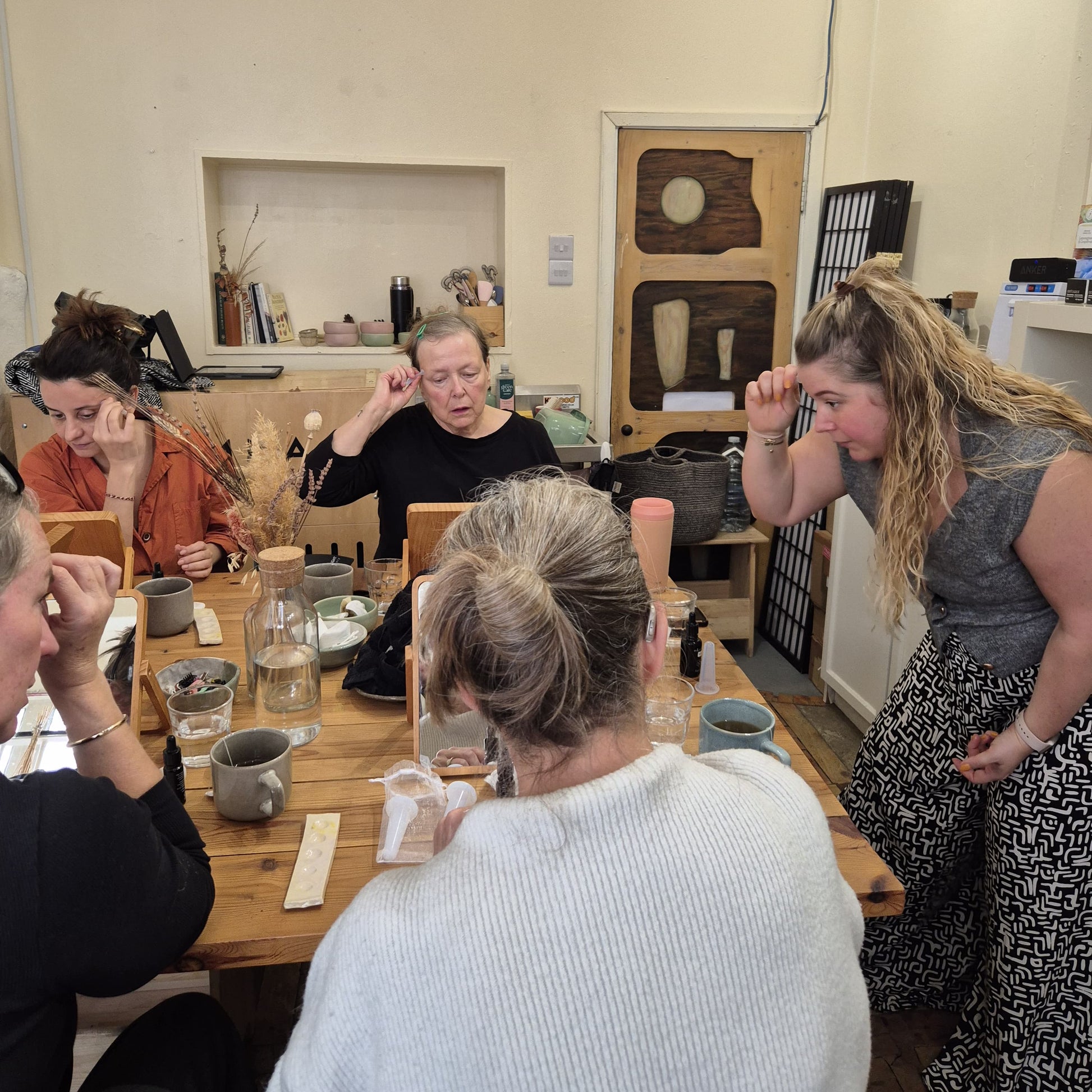 Group of people sitting around a wooden table in a casual setting, learning about organic skincare and how to use facial cups