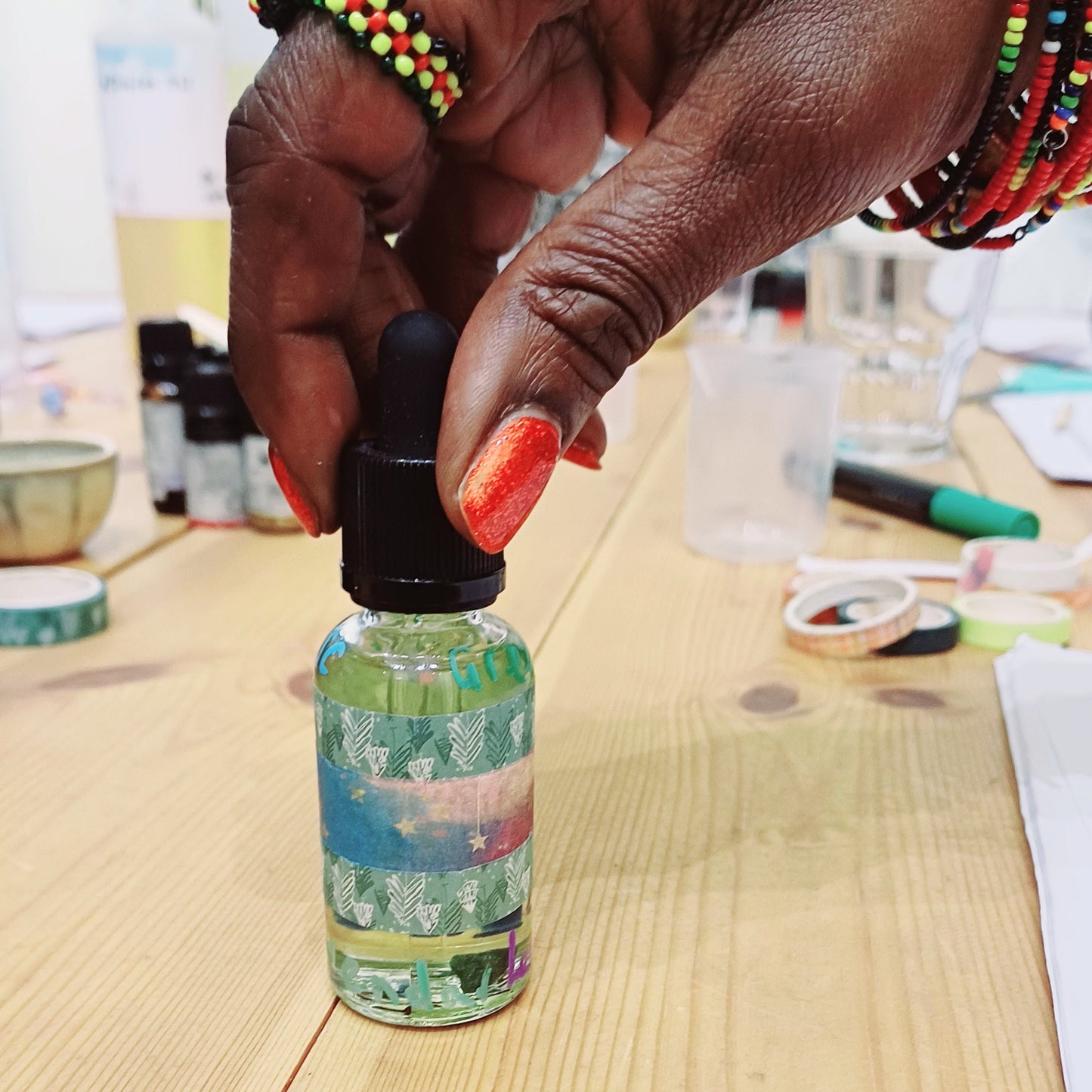 Hand holding a small bottle with a colorful label on a wooden surface.