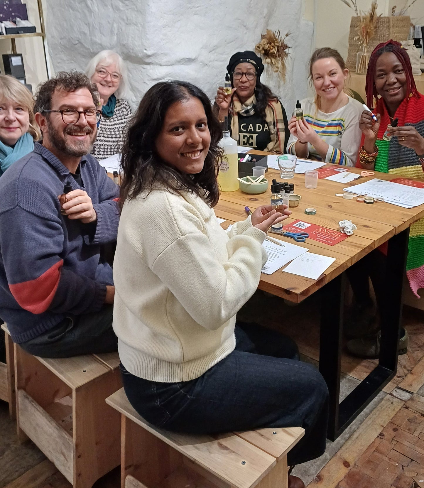 Group of people sitting around a table in a casual setting enjoying a facial oil making class in london