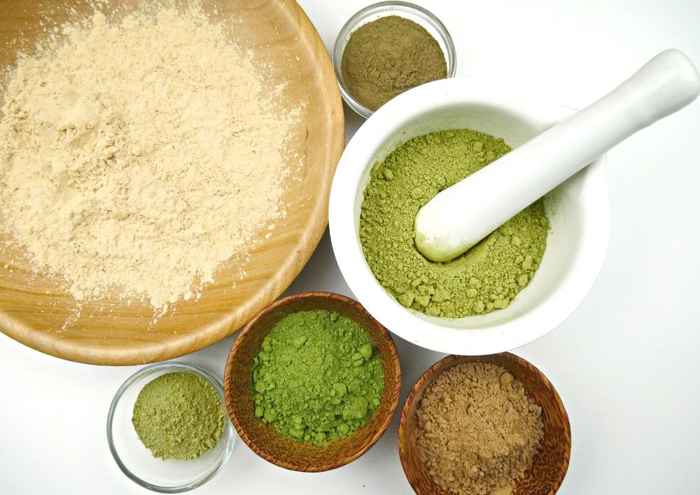 lifestyle image of natural henna based hair dye powders in wooden bowls and pestle and mortars. all the bowls are different sizes and the powders range from a light mustard yellow to a green brown to vivid green. used to demonstrate what the natural, organic hair dye looks like before it's blended with water