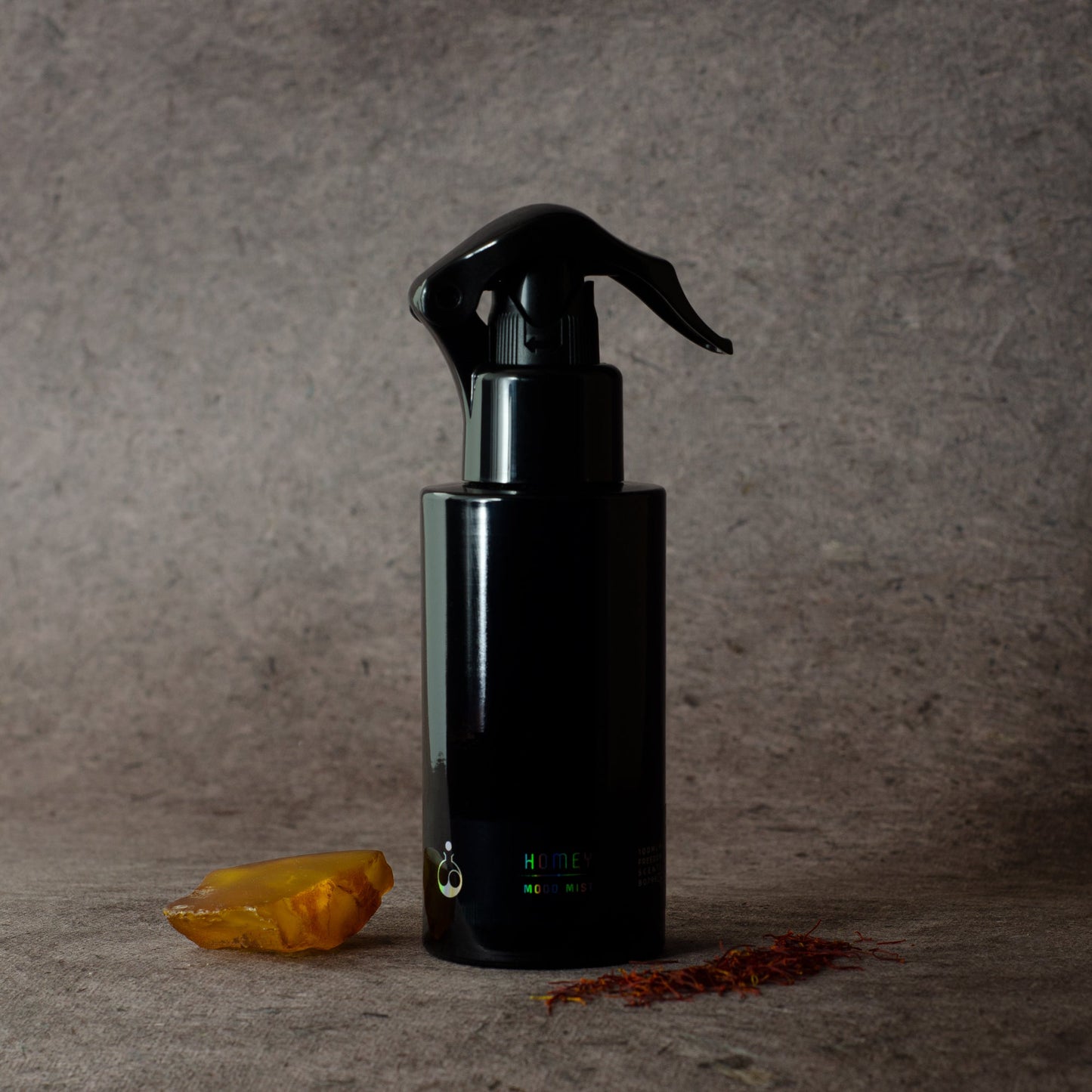 homey home fragrance on a grey background with amber and saffron next to the black pump bottle 