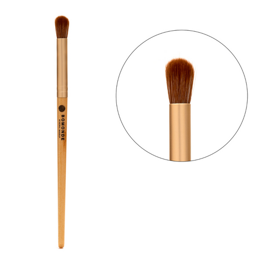 photo of bomonde's make up brushes. the brushes have a wooden bamboo handle, gold matte metal accent and the bristles are a chestnut coloured synthetic bristle that is certified cruelty free. the image shows the full length of the cruelty free make up brush on the left and in a circle to the right a close up of the bristles. this make up brush is a small fluffy eyeshadow brush which is used to apply eyeshadows, eye liners etc