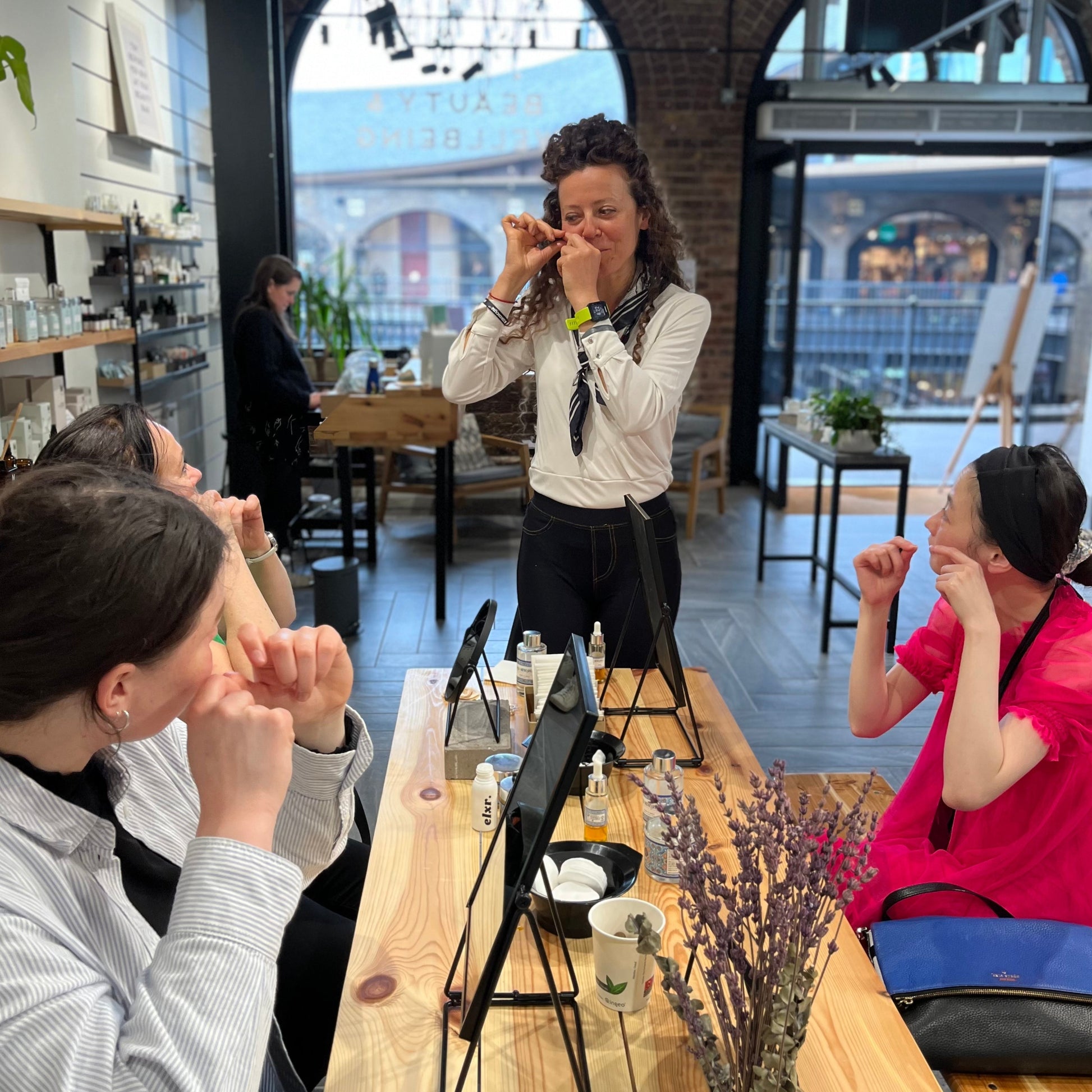 3 women sitting at a table looking towards lucia mencarelli from casa mencarelli organic skincare as she teaches them facial massage techniques they can do at home