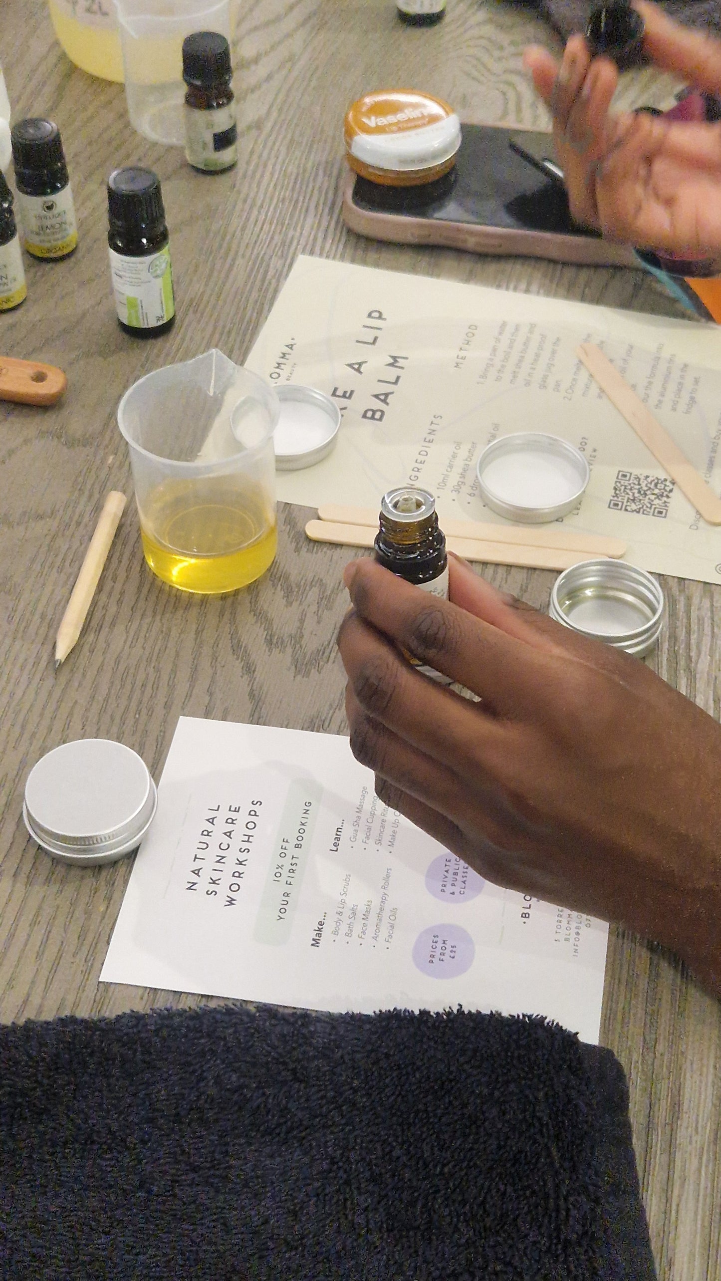person's hands holding a bottle of essential oils about to pour it into a beaker with oil as part of a lip balm making workshop in london