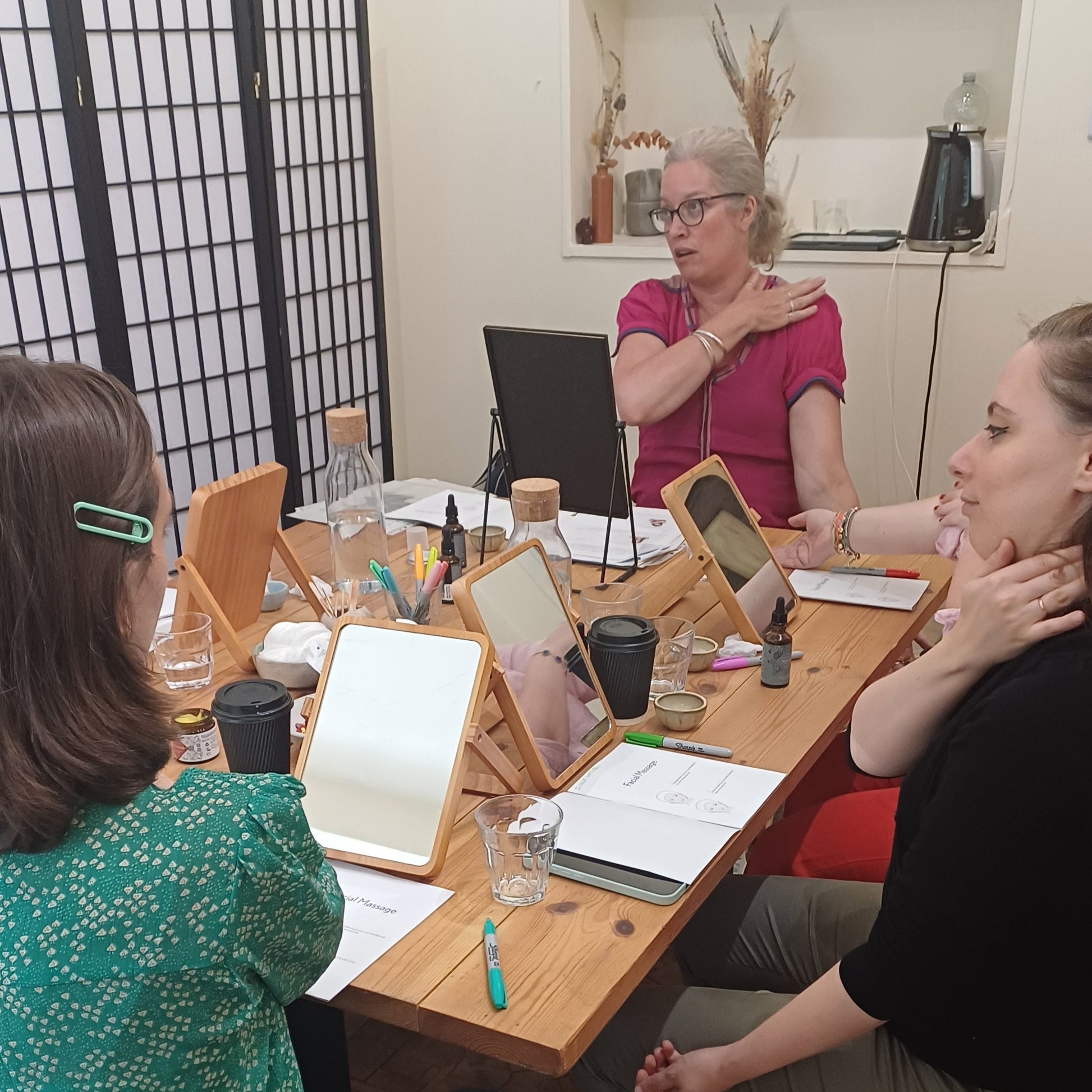 facial massage teacher marian dressing a pink top showing guests at a skincare masterclass in london how to massage their neck, shoulders, decollete and face to lift and tone the skin