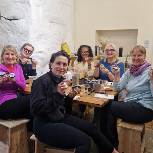group of people sitting around a table showing the products they made at a skincare making class 