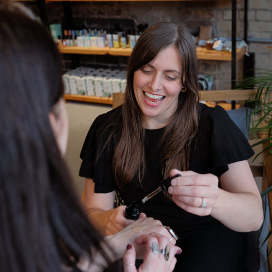 karen founder of blomma beauty in a black dress placing some face oil from a pipette onto a customers hand to try it