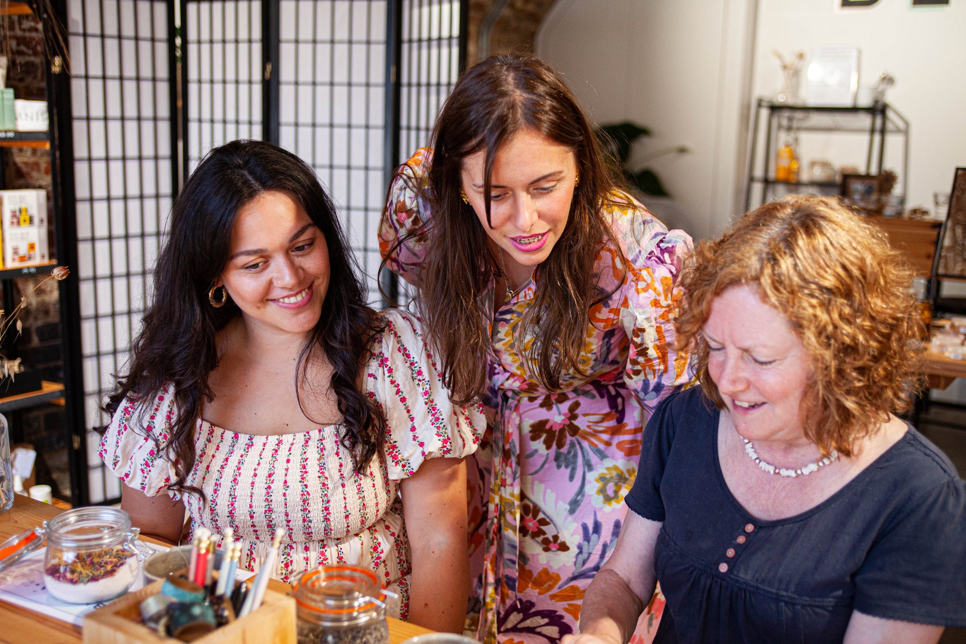 teacher leaning over 2 guests at a make your own skincare class in london