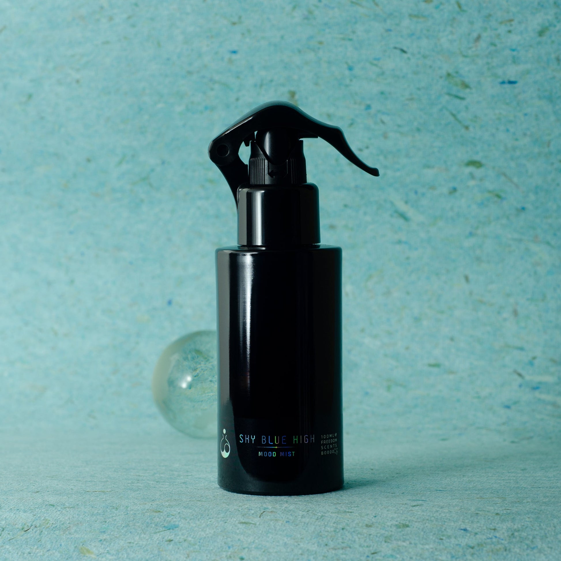Freedom scents mood mist room pillow and linen spray pictured on a turquoise background and a small marble. A black round bottle with a black pump spray and a black label with blue and white text.