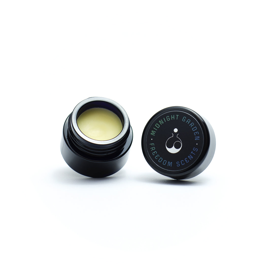 floriential solid perfume balm made in the uk. image is open black glass jar with lid open and fragrance balm inside 