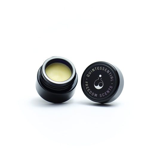 solid perfume in an open black glass jar on white background