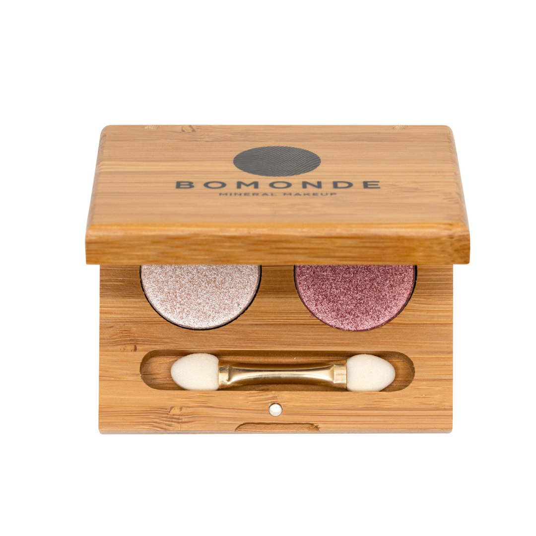 Aerial shot of Topazimite eyeshadow duo (shimmer nude and pink shadows). you can see the black text on the top of the bamboo refillable make up compact which reads 'bomonde mineral make up' with a partial view of the eyeshadows and brush