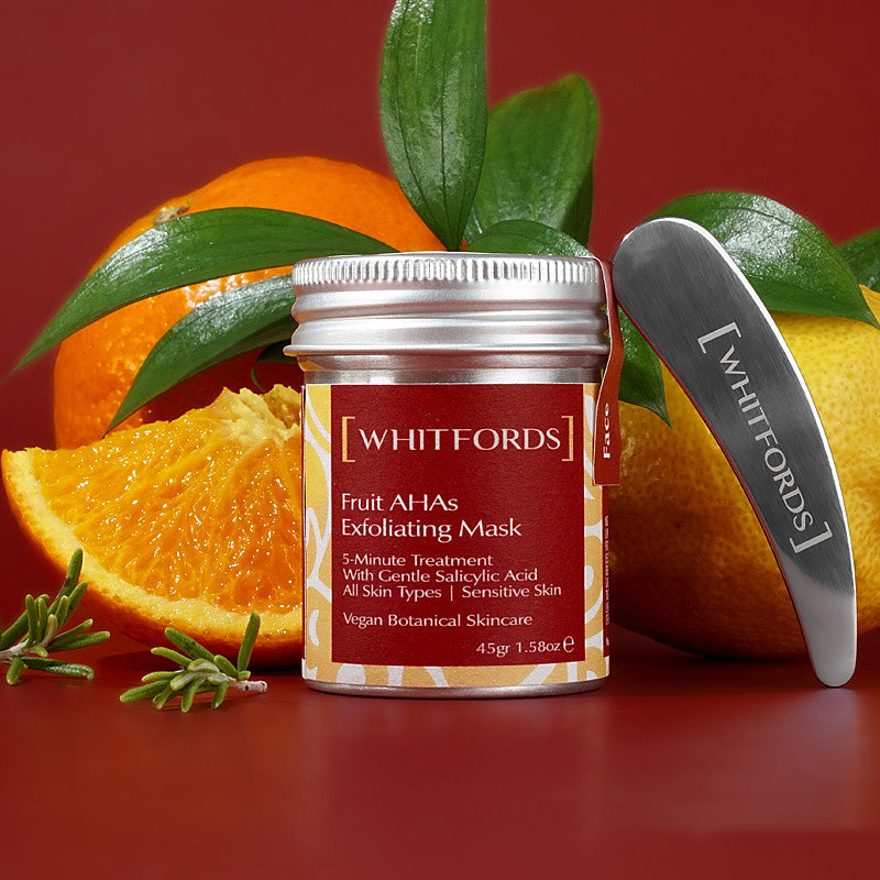 whitfords skincare granular and aha exfoliator in an aluminium tin with a red label on a red background and images of a metal spatula a whole lemon, orange, green leaves, rosemary fronds and an orange segment. the label reads 'whitfords fruit ahas exfoliating mask 5 minute treatment with gentle salicylic acid all skin types sensitive skin vegan botanical skincare'