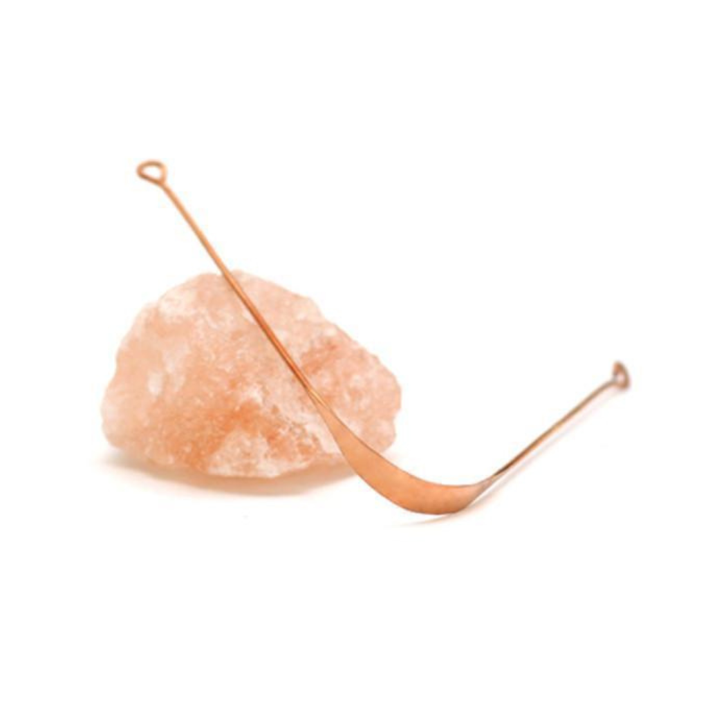 copper tongue scraper sitting on a piece of rose quartz
