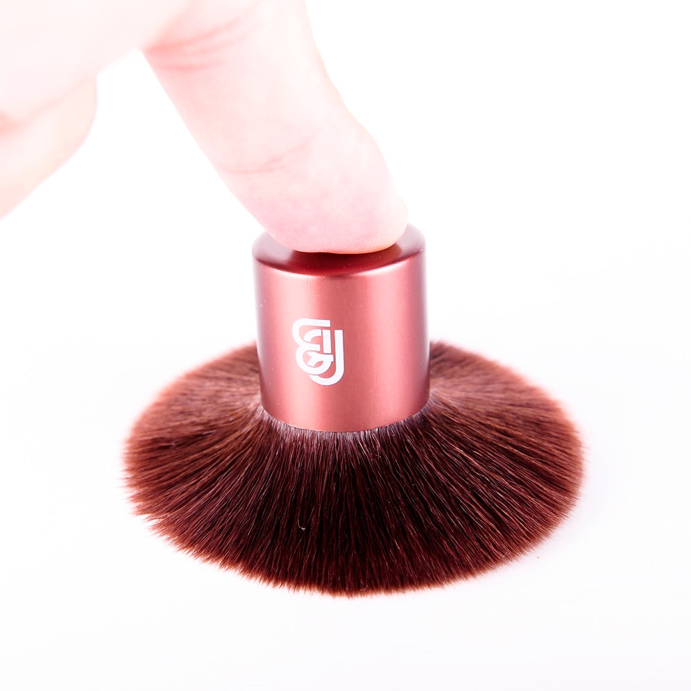 travel sized kabuki brush, placed upside down and being pushed down by a finger to show the width of the synthetic bristles 