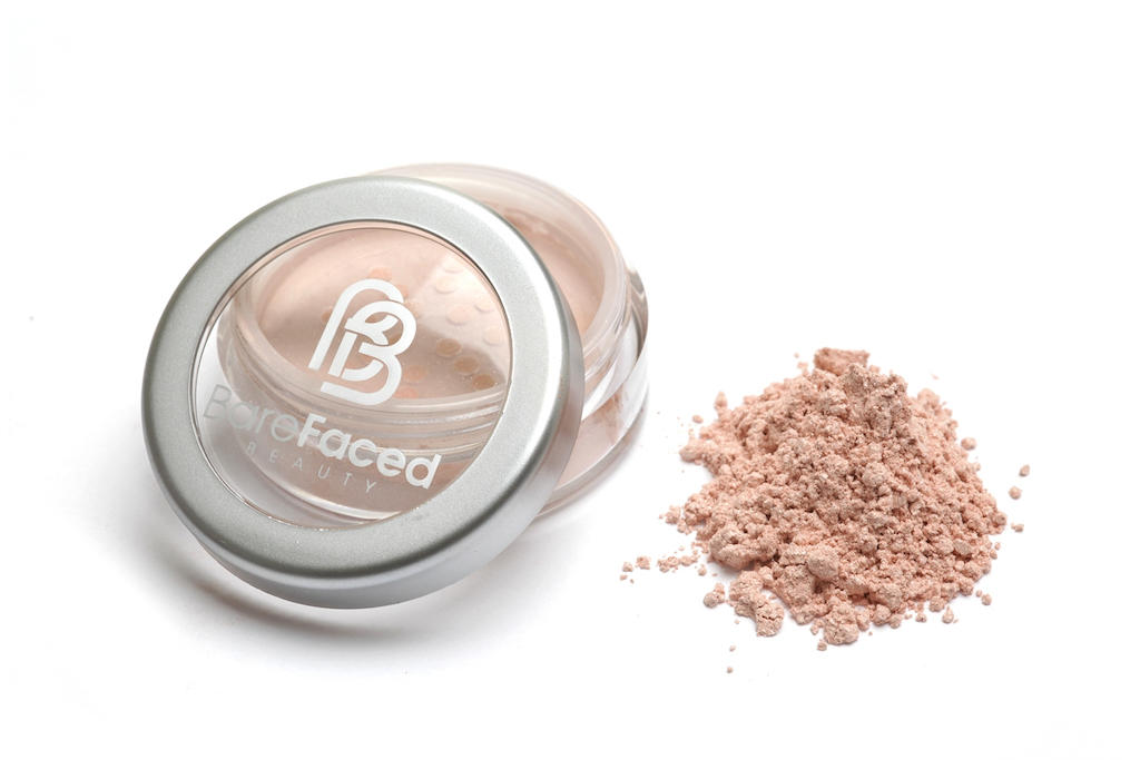 BareFaced Beauty Natural Mineral Shimmer in Cupid's Glow. Vegan highlighter makeup. The mineral shimmer is pictured in a plastic jar with a silver lid, and the logo in white on the lid. A pile of the shimmer is sitting next to the pot. The shade is a shimmery peachy pink.