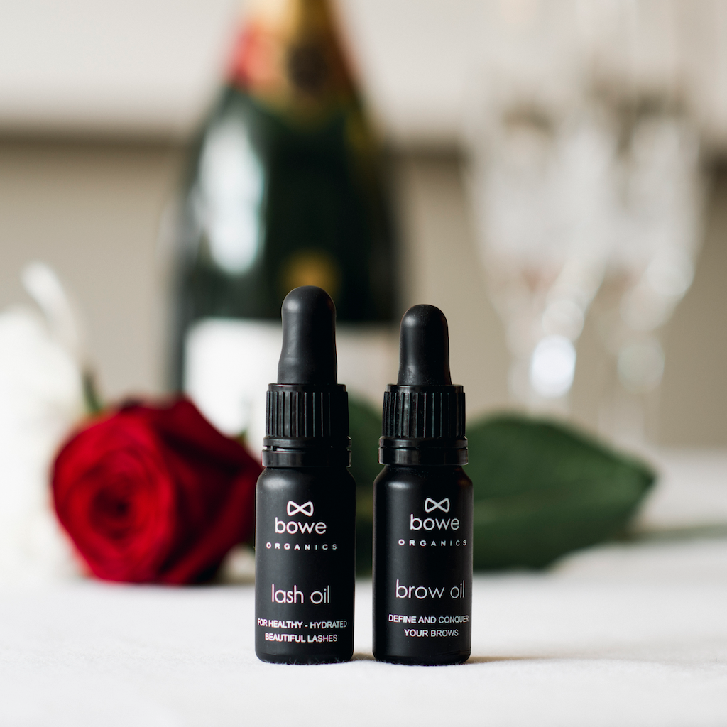 Bowe Organics Gift of Brows and Lashes. Vegan Valentines Gifts. The lash oil and brow oil are pictured next to each other, with a long stem rose and bottle of champagne in the background.