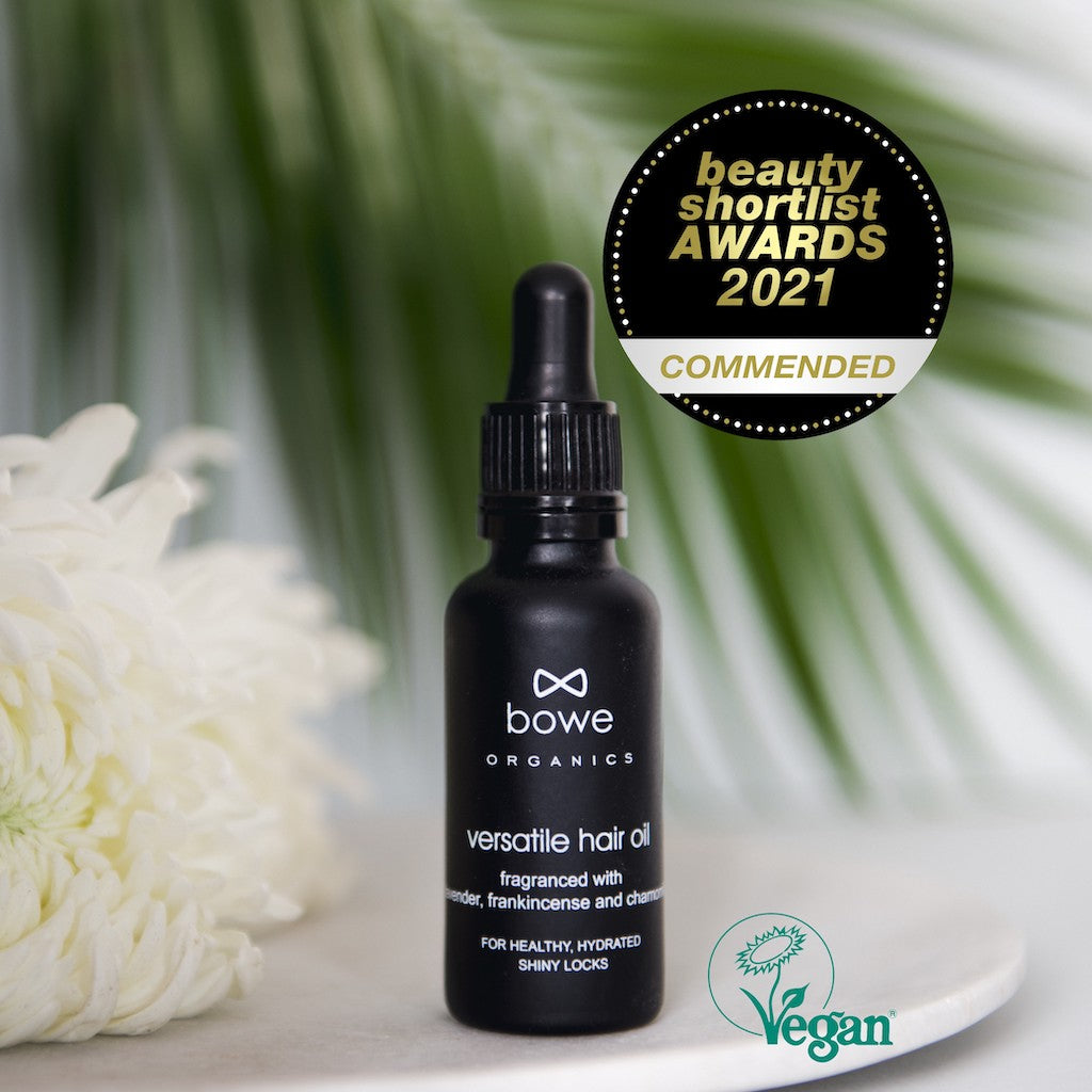 Bowe Organics Versatile Hair Oil Fragrance Free. Natural pre shampoo treatment. The oil is pictured in a black glass bottle with white text and a black pipette. There is a white flower and a palm leaf in the background. The image is overlaid with a Vegan Society logo and a Beauty Shortlist Awards 2021 Commendation.