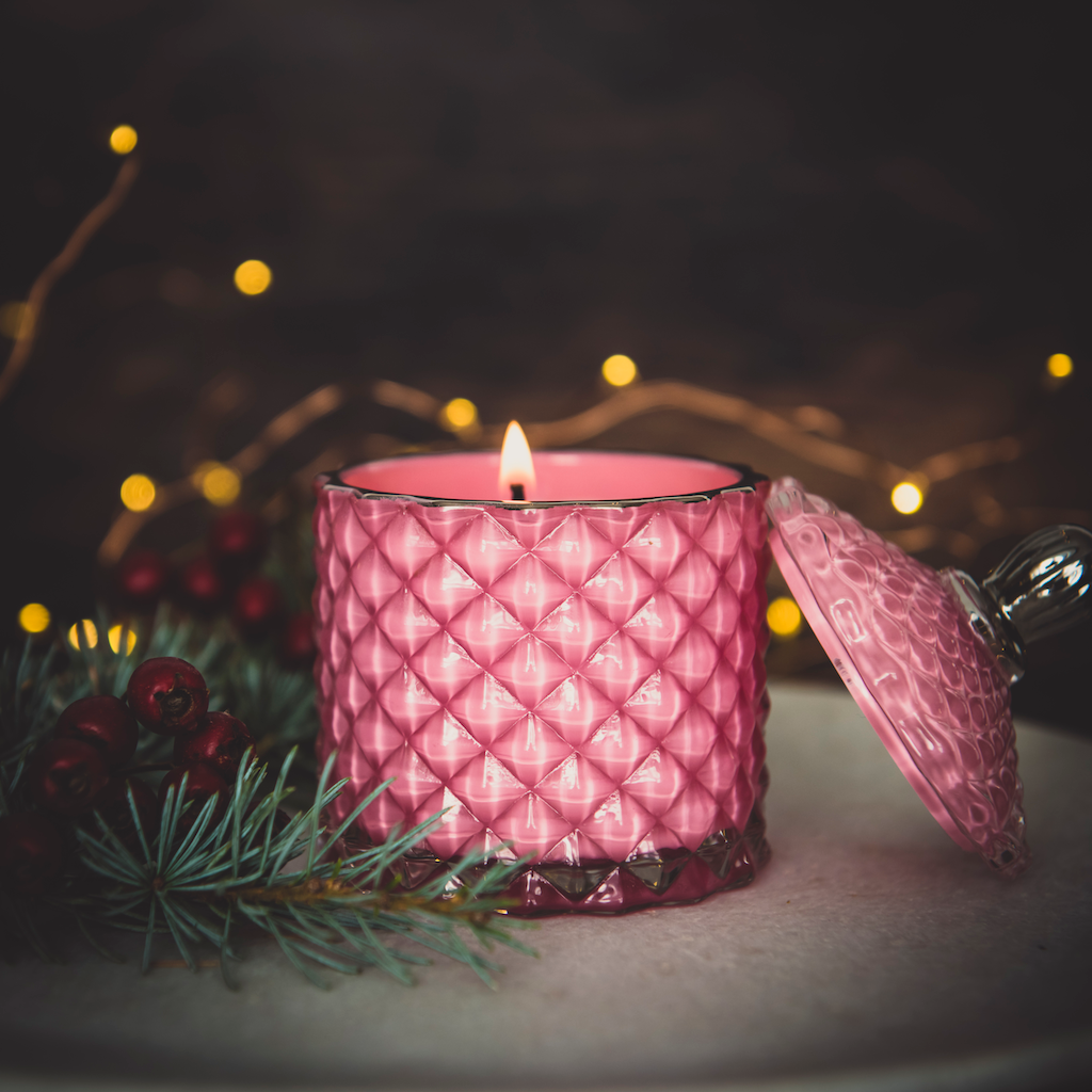 pink glass candle jar with lid off aflame with pine branch and twinkling lights 